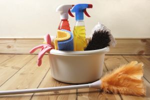 Bowl of cleaning products and feather duster on wooden floor