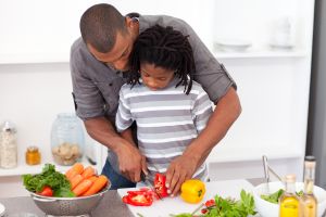 Loving father helping his son cut vegetables in the kitchen