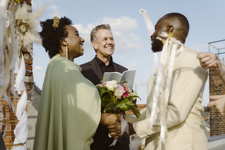 Smiling senior male minister looking at newly married couple at ceremony