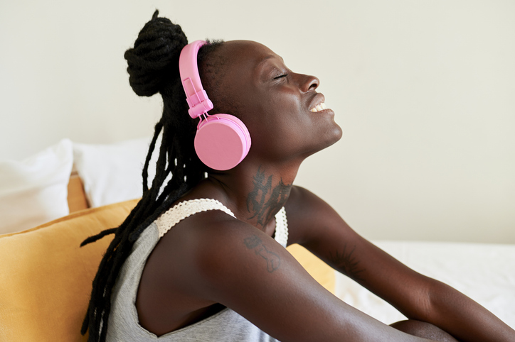 Woman wearing pink headphones enjoying music sitting on bed